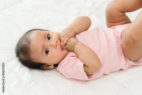 infant baby putting hands in mouth and sucking fingers on bed