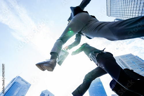 大都会で青空に向かって2人のチームで飛翔しジャンプするダイナミックで勢いのあるビジネスマンの男性