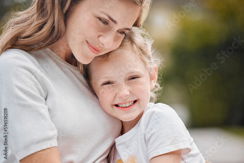 Closeup of loving caucasian mother giving her adorable daughter a hug while sitting outside on a sunny day. Young mom bonding outdoors with little girl