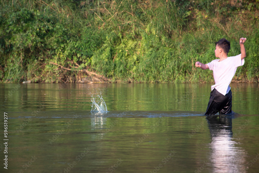 Asian boy in white t-shirt is spending his freetimes by diving, swimming, throwing rocks and catching fish in the river happily, hobby and happiness of children concept, in motion. Asian boy in white t-shirt is spending his freetimes by diving, swimming, throwing rocks and catching fish in the river happily, hobby and happiness of children concept, in motion.