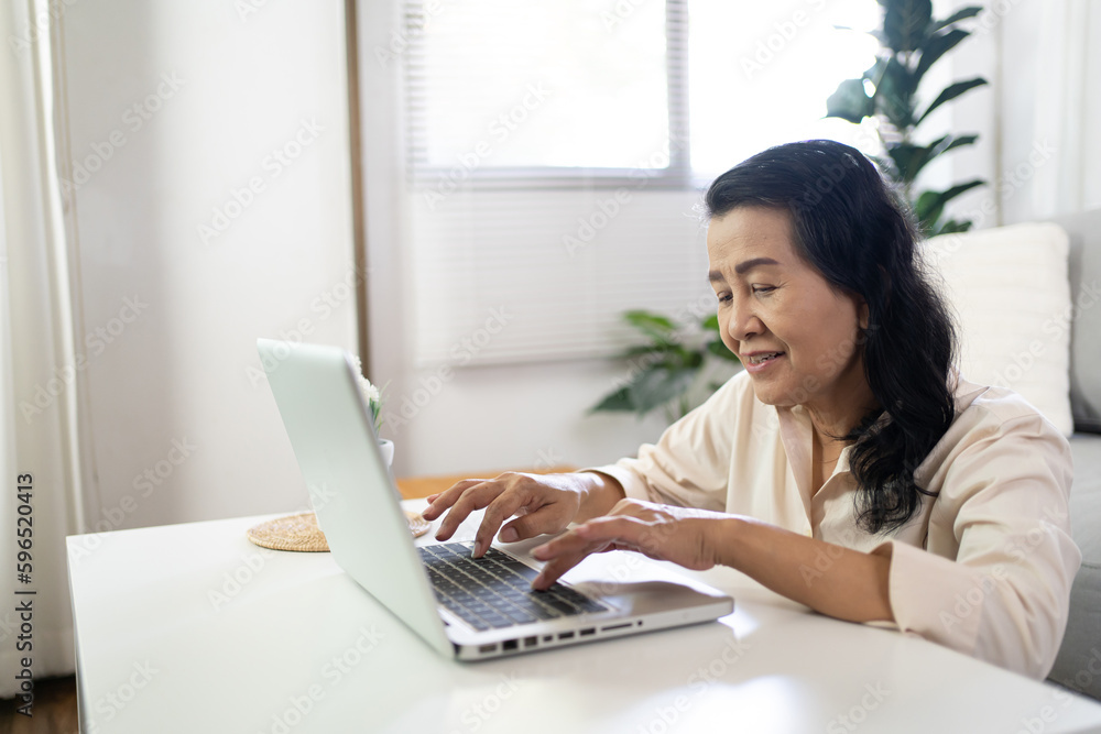 Middle age Asian woman Work from home. senior woman smiling Beautiful mature asian woman on laptop with technology concept Middle age Asian woman Work from home. senior woman smiling Beautiful mature asian woman on laptop with technology concept