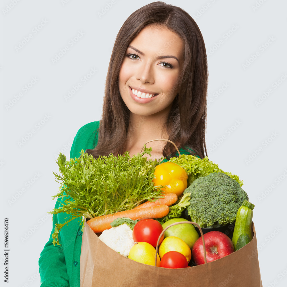 Square image of happy smiling woman in casual wear, green sweater with grocery shopping bag with vegetarian raw food vegetables, isolated light grey gray background. Healthy eating, dieting concept. Square image of happy smiling woman in casual wear, green sweater with grocery shopping bag with vegetarian raw food vegetables, isolated light grey gray background. Healthy eating, dieting concept.