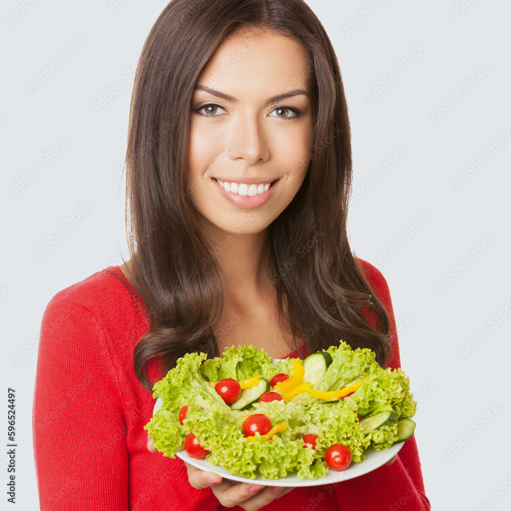 Square image of smiling young asian caucasian woman in red casual cloth, sweater, holding salad plate, isolated grey gray background. Brunette girl. Keto ketogenic dieting, weight loss, healthy eat.