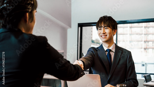 オフィスの会議室で笑顔で握手をする中小企業やスタートアップのビジネスマンの男性2人 photo