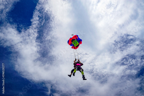 Tandem skydiver pair open parachute in the clouds