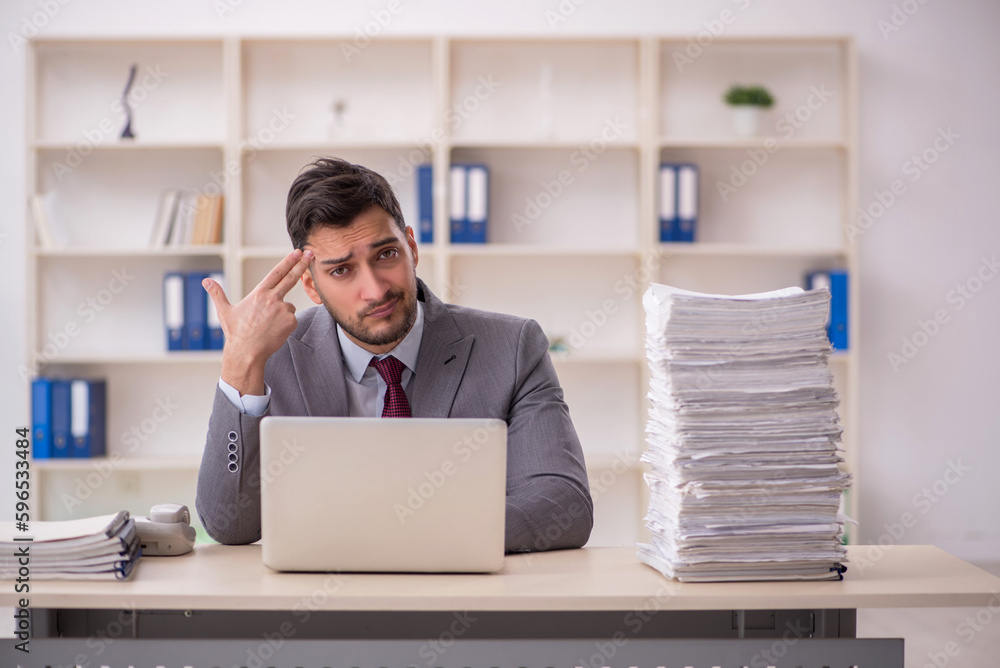 Young male employee unhappy with excessive work in the office Young male employee unhappy with excessive work in the office