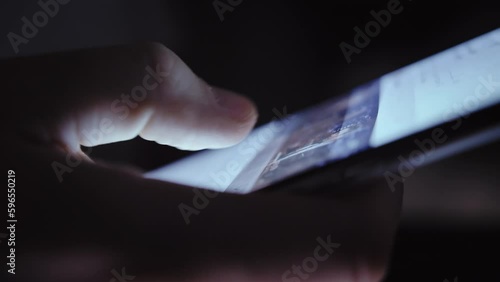 In the Dark: Close-Up of Man Scrolling Screen on Phone with Glare photo