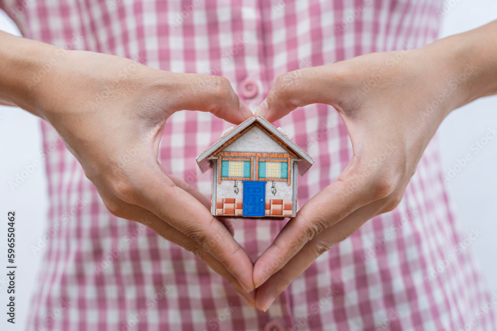 Purchase and sale of real estate, construction of a residential building. A woman's hand holds a mock-up or miniature of a residential building. Purchase and sale of real estate, construction of a residential building. A woman's hand holds a mock-up or miniature of a residential building.