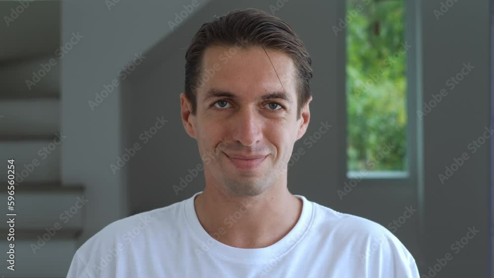close-up portrait of a millennial man in a white t-shirt looks at the camera and smiles against the backdrop of a home interior or office. satisfied man 30 years old looking at the camera with a smile close-up portrait of a millennial man in a white t-shirt looks at the camera and smiles against the backdrop of a home interior or office. satisfied man 30 years old looking at the camera with a smile
