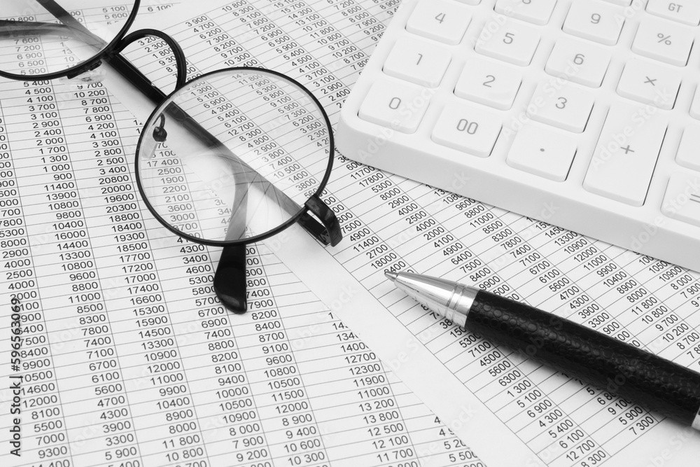 Round glasses, black pen and white calculator on statements data. Accountancy and statistics concept. Round glasses, black pen and white calculator on statements data. Accountancy and statistics concept.