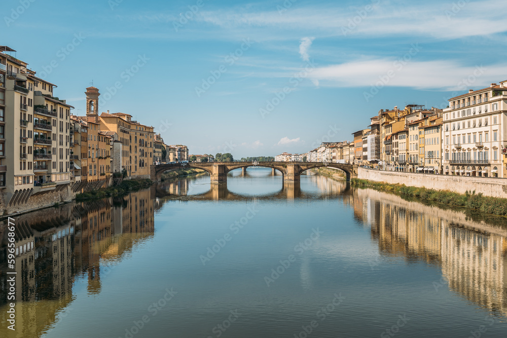 Gorgeous view of an old stone bridge across a river in Italy on a sunny warm summer evening on a blue sky. The concept of historical important infrastructural structures in Europe. Copyspace
