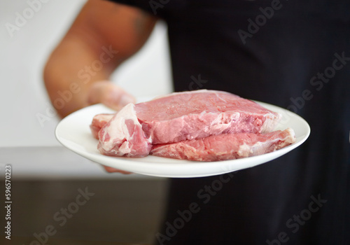 Food, protein and a plate of raw steak in the hand of a man for diet, nutrition or meal preparation. Kitchen, cooking and meat with a strong male bodybuilder eating beef for a healthy lifestyle