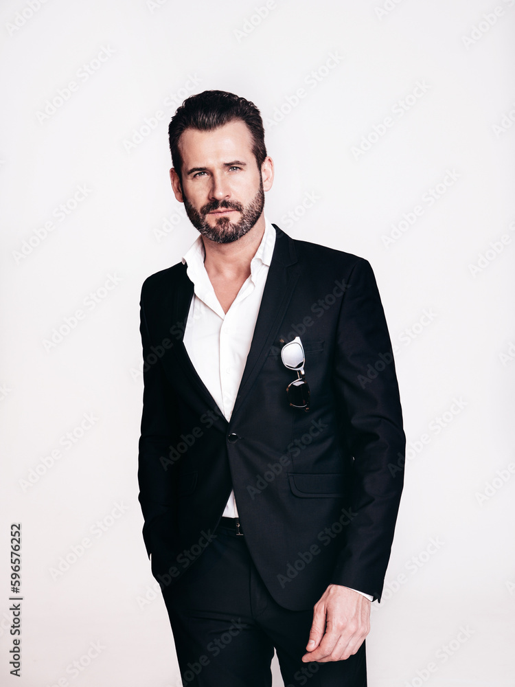 Fototapeta premium Portrait of handsome confident stylish hipster lambersexual model. Sexy modern man dressed in black elegant suit. Fashion male posing in studio, isolated on white