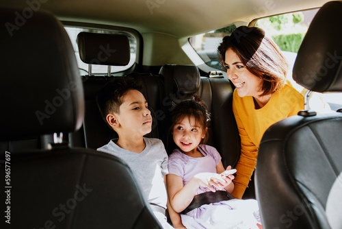 latin mother put her daughter and son in a car seat and fastens her seat belts for protection during the trip in the car in Mexico, hispanic family