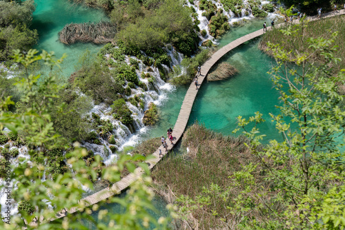 People walking a wooden path through turquoise water in Plitvice national park - Croatia