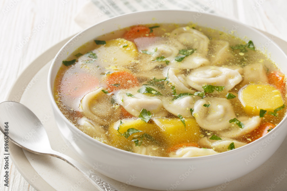 Delicious dumplings soup with carrots, onions, potatoes and chicken broth close-up in a plate on a wooden table. Horizontal