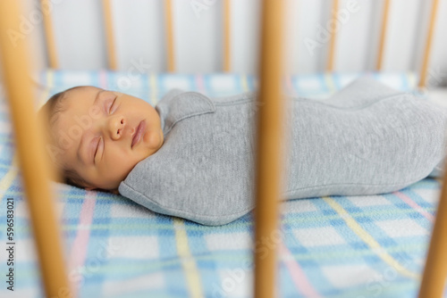 The baby is lying in a cocoon on cot. He sleeps sweetly and dreams.