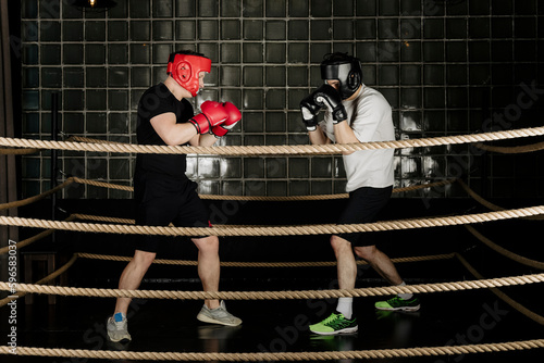 Two big guys boxing and sparring in the ring in head guard helmets and gloves.