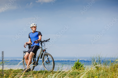 Young man cycling on a rural road through green spring meadow