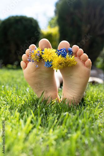 bare feet ofchild lying on bright juicy green grass. wreath of yellow-blue field flowers lies on the toes. joy, cheerful positive atmosphere, carelessness, happy childhood. Hello summer, holidays photo