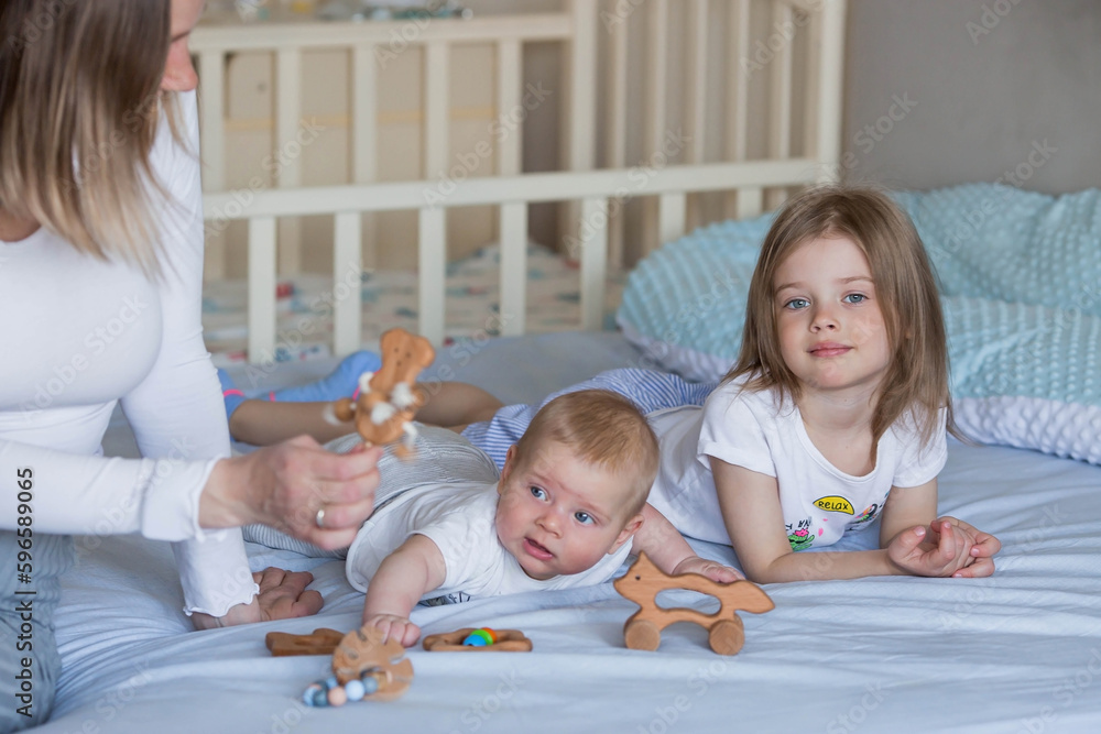 Family, childhood and love. A little girl and a mom in bed in a bright bedroom playing with her younger newborn brother. Children, motherhood. Family, childhood and love. A little girl and a mom in bed in a bright bedroom playing with her younger newborn brother. Children, motherhood.