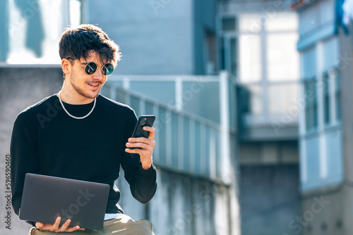 young male with mobile phone and laptop outdoors