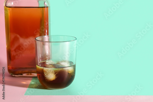 Glass and bottle of rum with ice cubes on colorful background