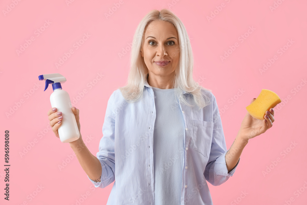 Mature woman with cleaning sponge and detergent on pink background Mature woman with cleaning sponge and detergent on pink background