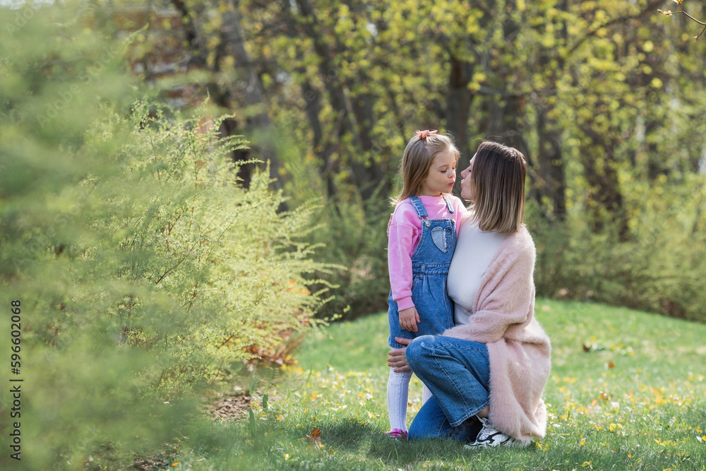 Fototapeta premium A beautiful little girl in pink clothes walks with her mother in the park in the fresh air. Family, children, motherhood.