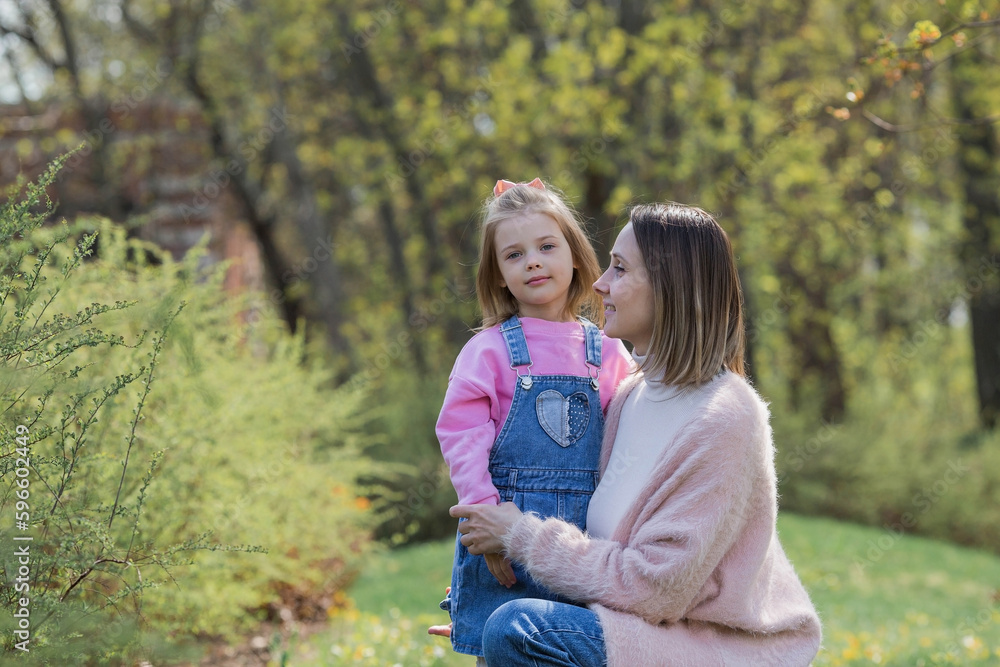 Fototapeta premium A beautiful little girl in pink clothes walks with her mother in the park in the fresh air. Family, children, motherhood.