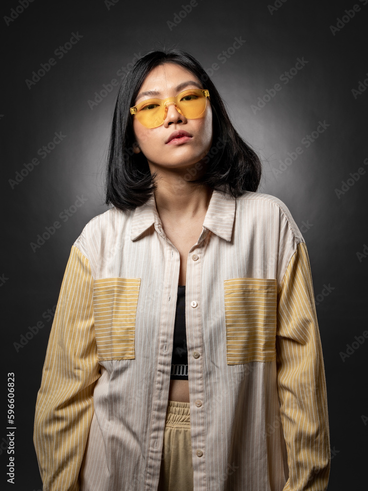 A portrait of an Asian girl wearing yellow glasses with a casual fashion style posing with a hip hop style. A portrait of an Asian girl wearing yellow glasses with a casual fashion style posing with a hip hop style.