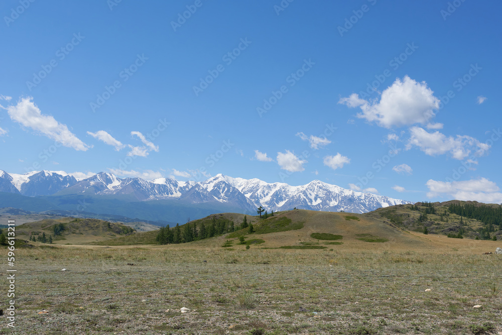 Panoramic view of snow-capped mountain peaks against a blue sky with clouds. Picturesque nature wallpaper.