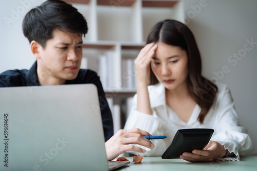 Asian couple sitting at table at home, using laptop to check documents overdue bills, taxes, debt due, bank account balance.lack of money bankruptcy, financial problems concept.