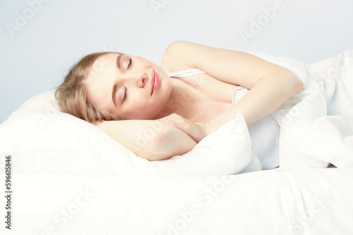 Photo of sleeping young woman lies in bed with eyes closed.