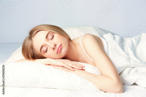 Photo of sleeping young woman lies in bed with eyes closed.