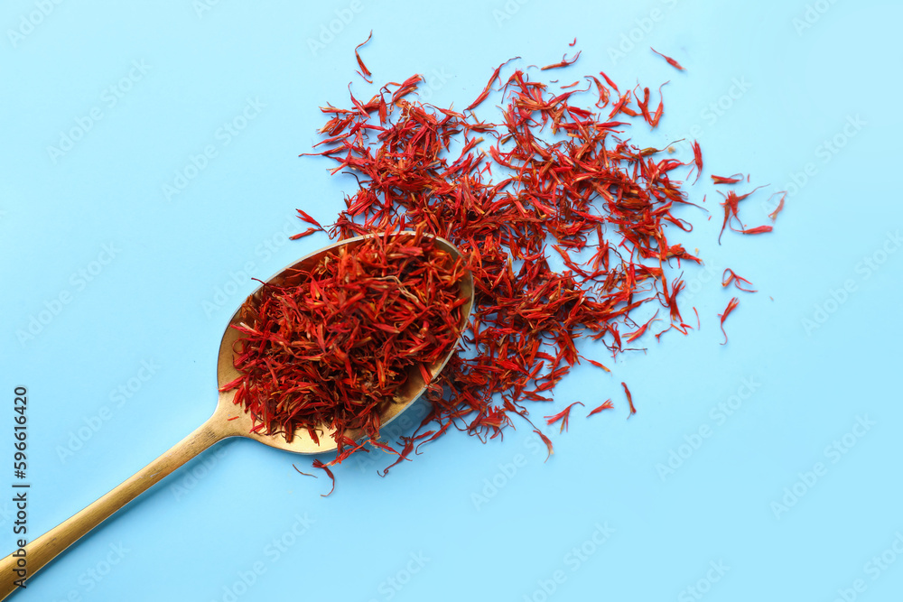 Fototapeta premium Spoon with pile of saffron on blue background