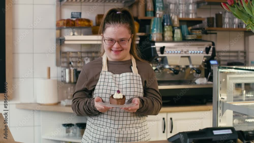 Portrait of down syndrome girl as a worker in the cafe who is holding a piece of cake. Shot with RED helium camera in 8K. Portrait of down syndrome girl as a worker in the cafe who is holding a piece of cake. Shot with RED helium camera in 8K.
