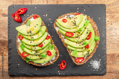 Avocado toasts - bread with avocado slices, pieces of red pepper and sesame on black stone board.