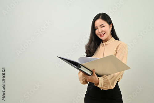 Confident asian businesswoman holding open binder standing over gray background. Copy space for your text