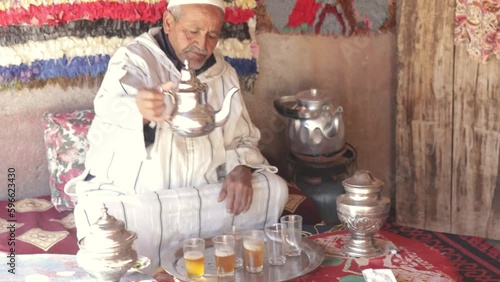 Moroccan senior man in traditional dress serving mint tea with silver utensils on terrace