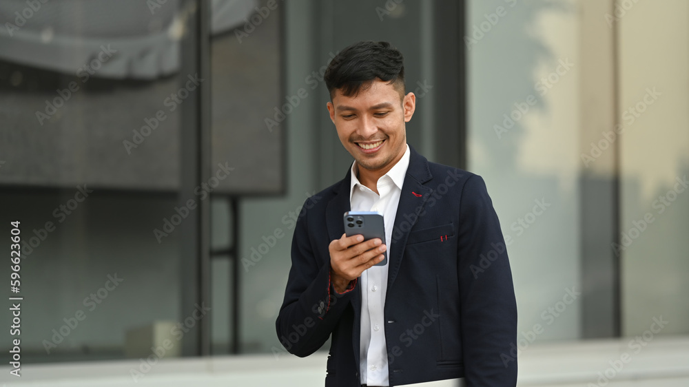 Millennial businessman using smartphone while sitting outside office building. Modern lifestyle and technology concept Millennial businessman using smartphone while sitting outside office building. Modern lifestyle and technology concept