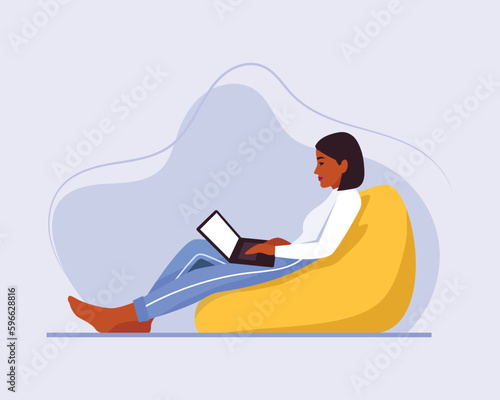 dark-skinned girl with short hair sits on a bean bag chair with a laptop