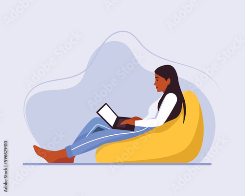 dark-skinned girl with long hair sits on a bean bag chair with a laptop