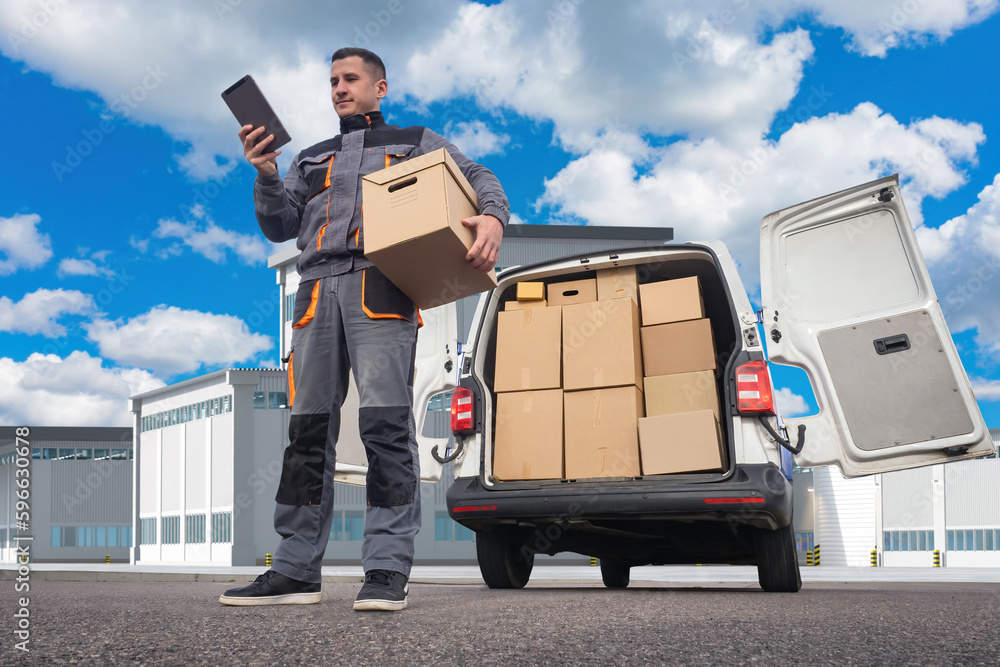 Deliveryman. Man courier with tablet. Employee of logistics company near  minivan. Courier under blue sky. Man works in delivery service. Transport  company agent. Courier on territory of enterprise Stock Photo | Adobe