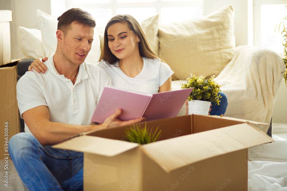 Young couple holding album while sitting on floor in new house. Young couple holding album while sitting on floor in new house.