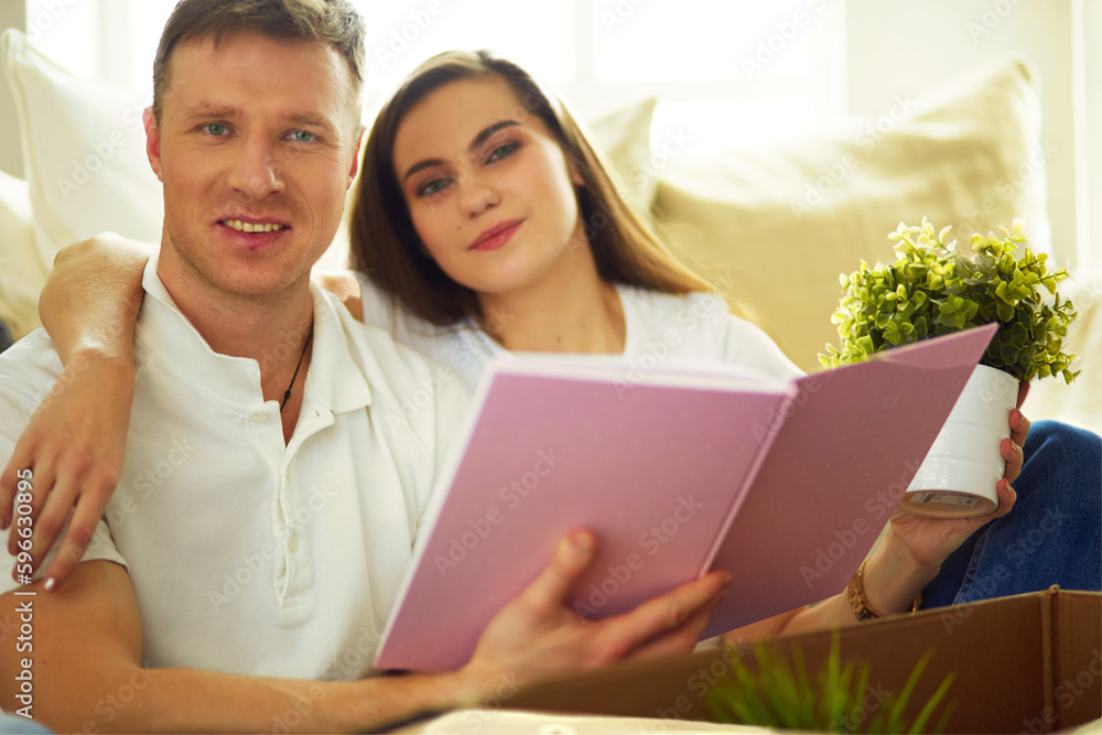 Happy couple looking at photo album while unpacking stuff after relocation to new flat. Happy couple looking at photo album while unpacking stuff after relocation to new flat.
