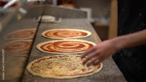 Side angle of unrecognizable male pizza chef decorating three pizzas with grated cheese standing in front of grey marble kitchen table in pizzeria 