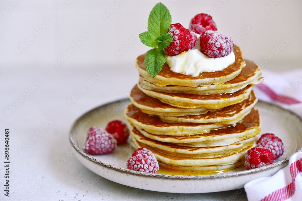Delicious homemade pancakes with whipped cream, maple syrup and raspberry for a breakfast.