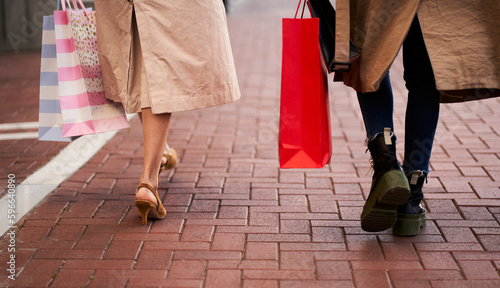Rear view of two unrecognizable women walking outdoors holding shopping bags. Friends buying clothes and gifts on sale discounts.