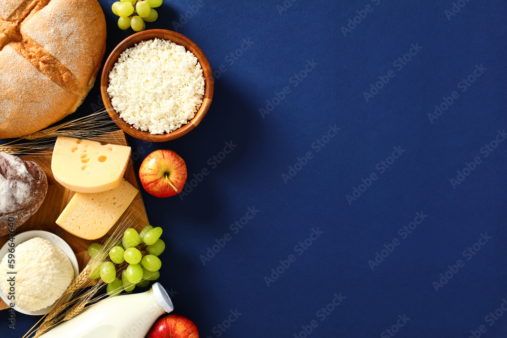 Happy Jewish holiday Shavuot greeting card template. Flat lay cottage cheese, grape, bread, apple, wheat, cheese on blue background. - obrazy, fototapety, plakaty 